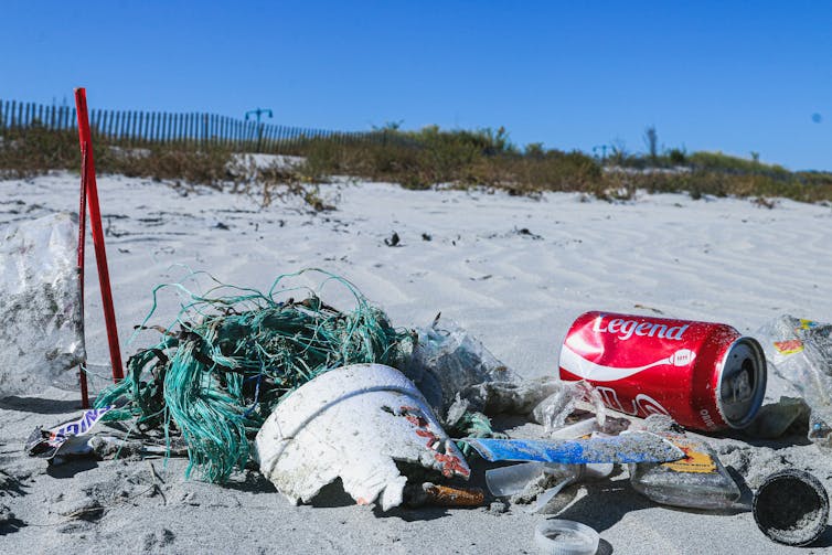 Plastic pollution and a red drink can on a beach.