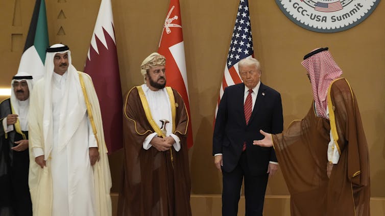 Four men stand in front of flags.