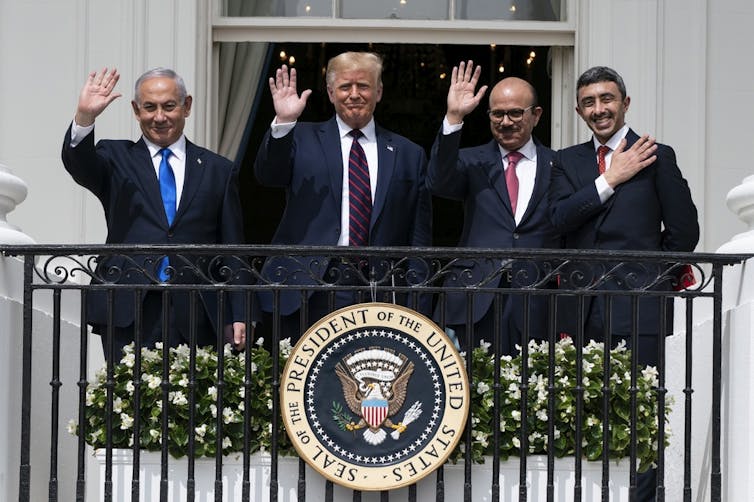 Four men wave from a balcony.