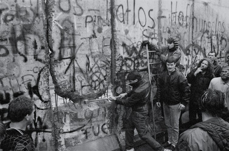 Men with pickaxes stand next to a wall covered in graffitti.