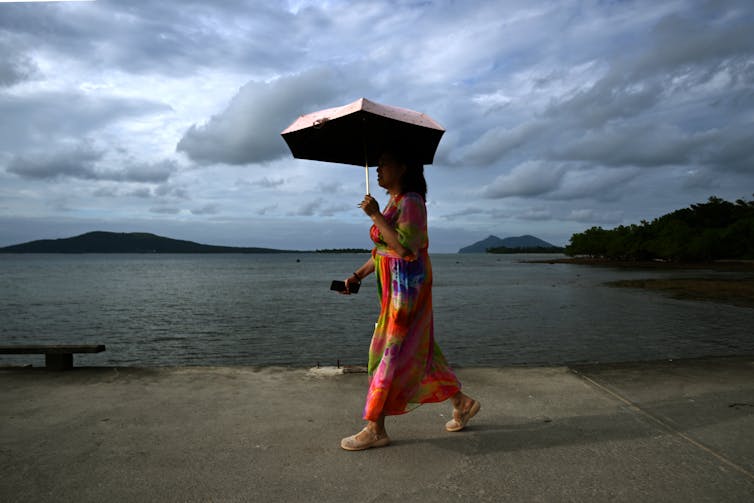Woman in a red dress walking along a wharf holding an umbrella.