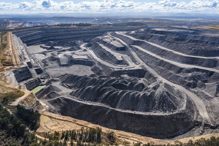 a high view of an open cut coal mine, with piles of coal and roads visible.