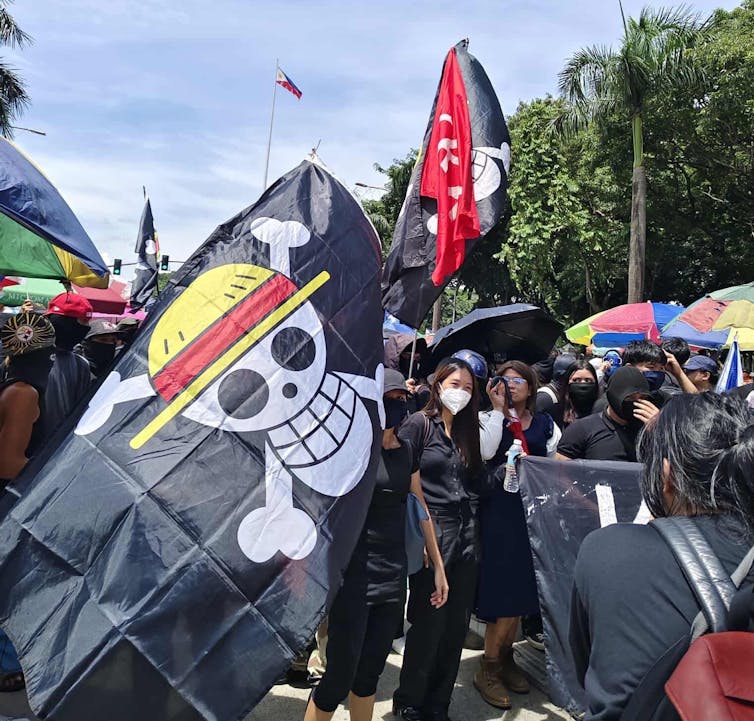 A large flag with a skull and crossbones on it is surrounded by people.