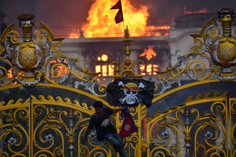 A skull-and-crossbones flag is seen in front of a blazing building