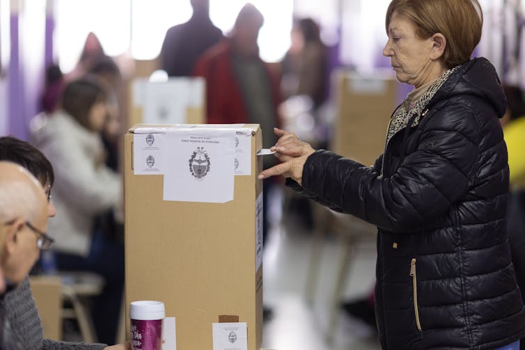 A woman casts a vote into a box.