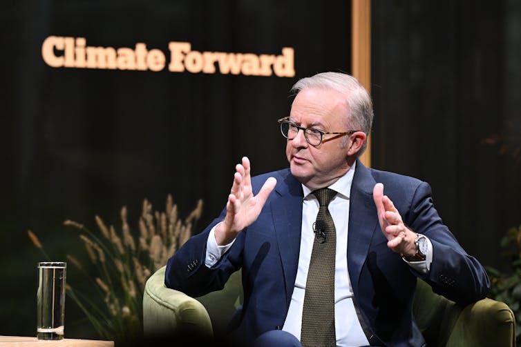 A man in a suit gestures in front of a sign reading 'Climate Forward'