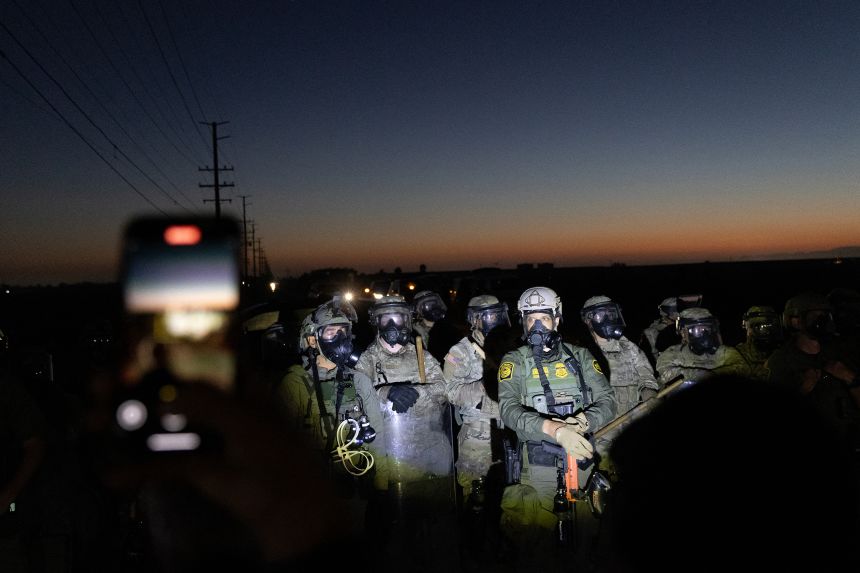 Customs and Border Protection officers and California National Guard troops stand as protestors shine flashlights on them after federal immigration agents conducted a raid on Glass House Farms in Camarillo, California, on July 10, 2025.