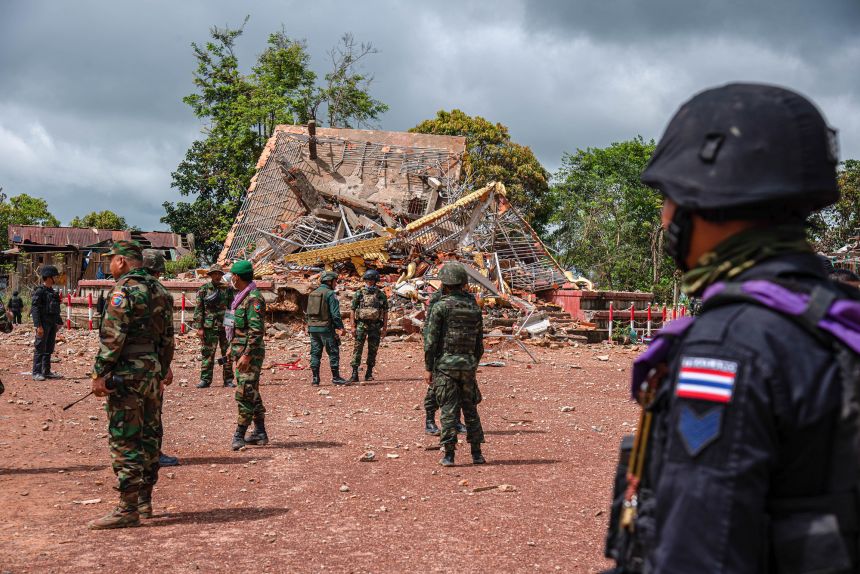 Cambodian and Thai soldiers stand guard near a destroyed building during the ASEAN Interim Observer Team visit to the Chong An Ma area in Ubon Ratchathani.