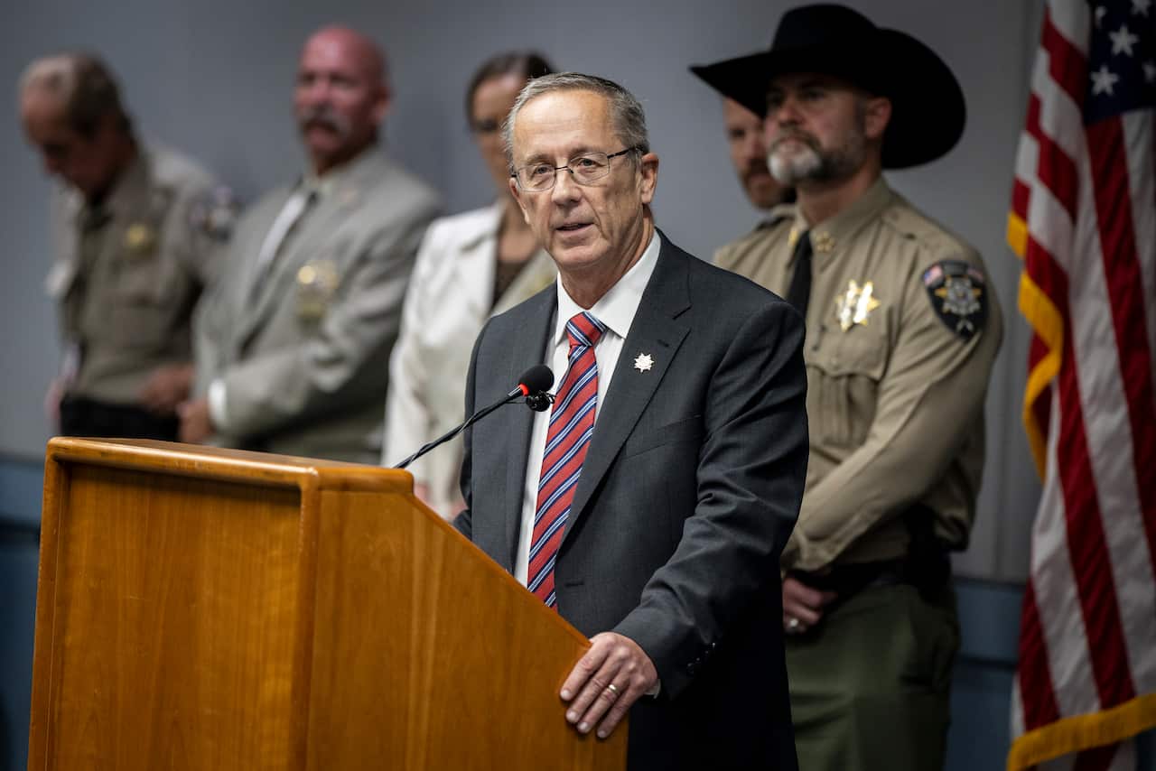 A man in a suit speaking at a lectern with people standing behind him