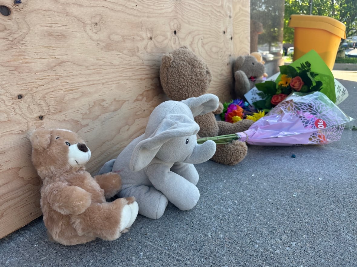 Stuffed animals and flowers are on the ground leaning against a wall.