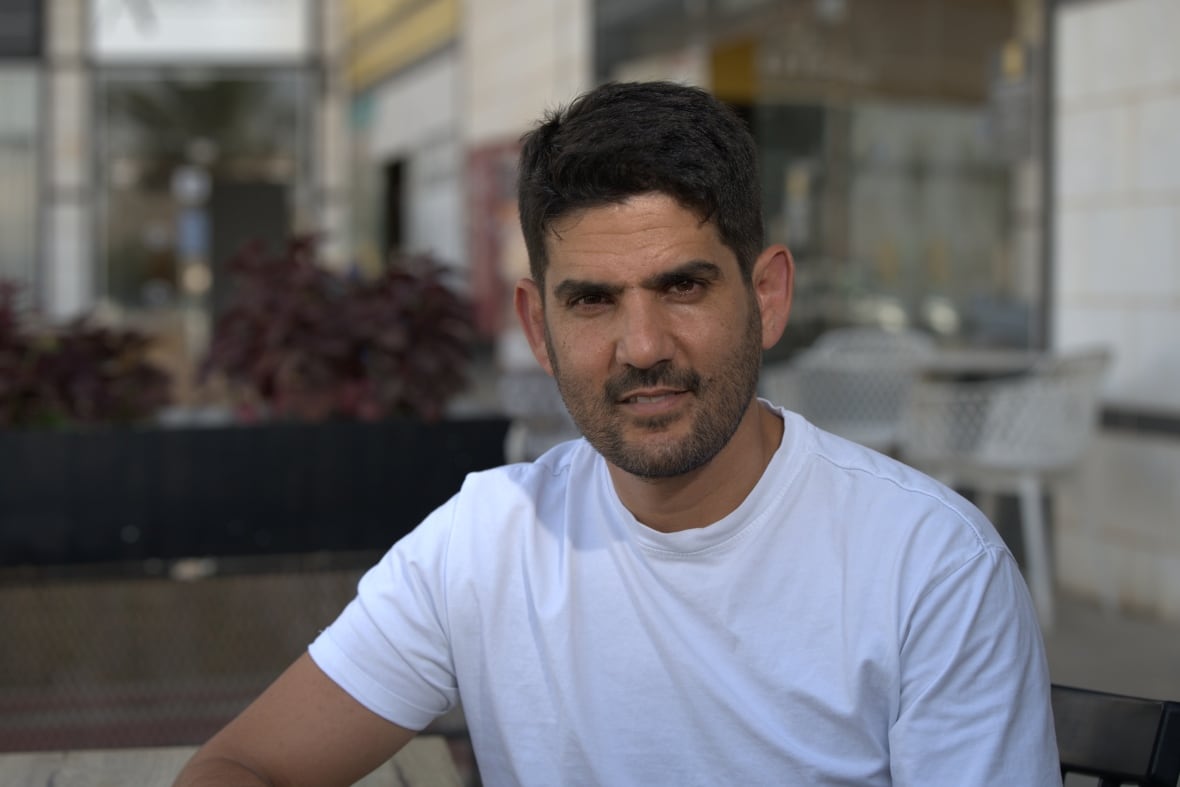 A man in a white T-shirt sits outside.