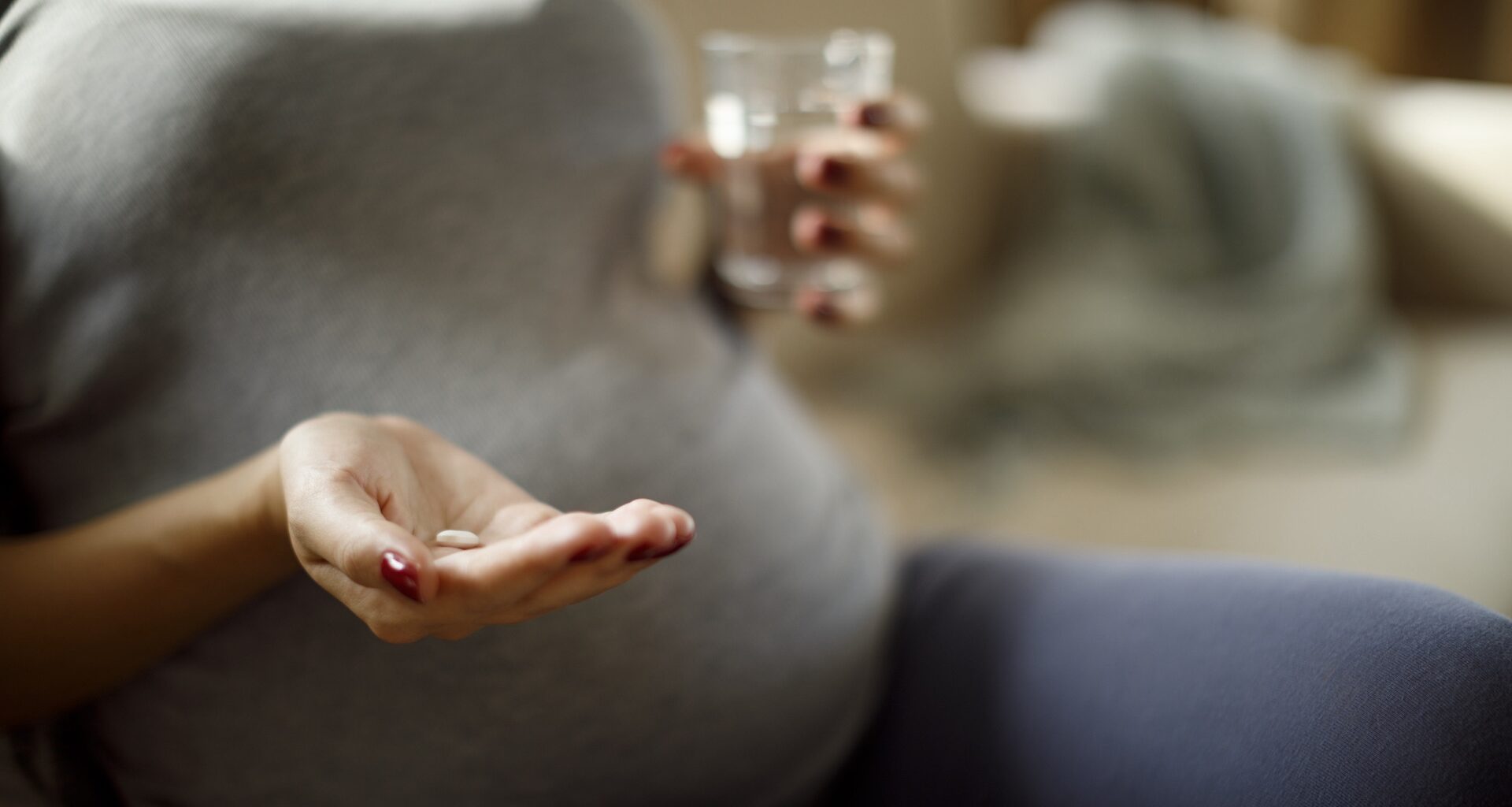 Closeup on belly of pregnant woman, who is holding a pill and water glass