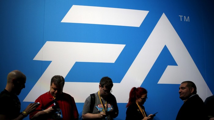 Attendees stand in front of a large Electronic Arts (EA) logo at the Electronic Entertainment Expo (E3).