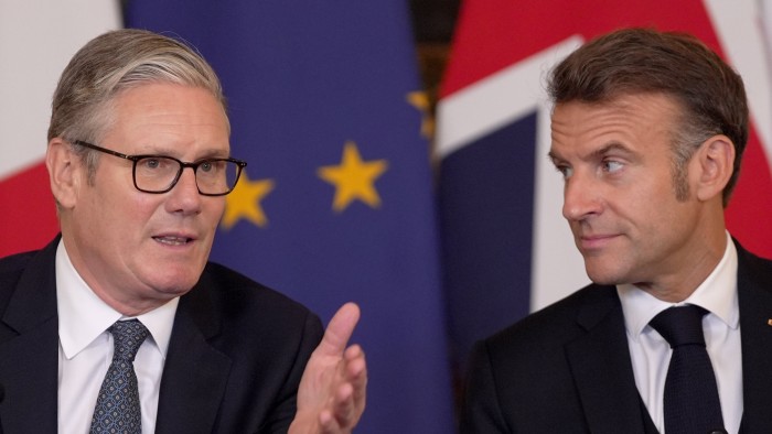 UK Prime Minister Sir Keir Starmer gestures while speaking as President Emmanuel Macron looks on, with UK and EU flags behind them.