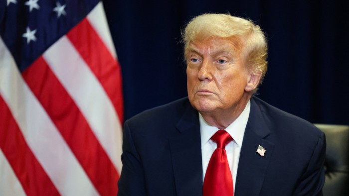 Donald Trump sits in front of an American flag, wearing a dark suit and red tie, during a meeting at the United Nations General Assembly.