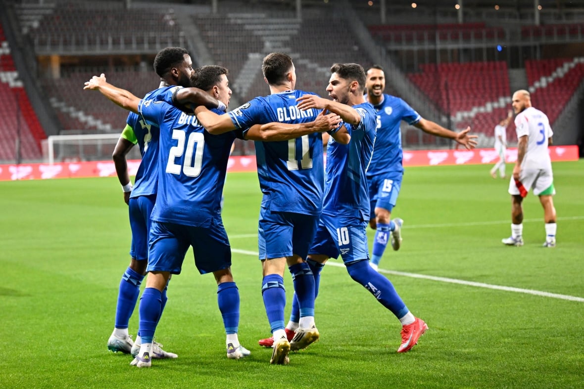 Men in blue soccer uniforms embrace on a soccer pitch