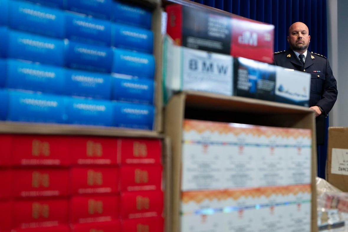 A man in a police uniform looks at piles of cigarettes.