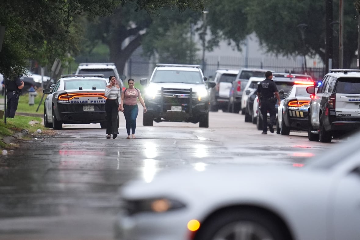 People walk along a road lined by cars.
