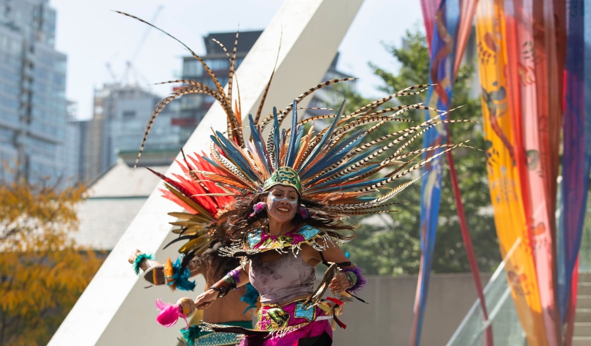 An indigenous dancer in bright colours and a long feather headdress dances smiling.