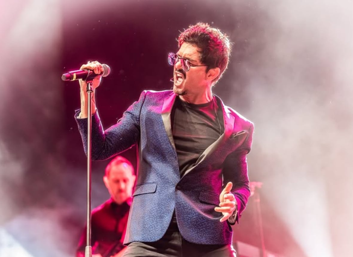 A singer wearing a purple blazer is shown on stage.
