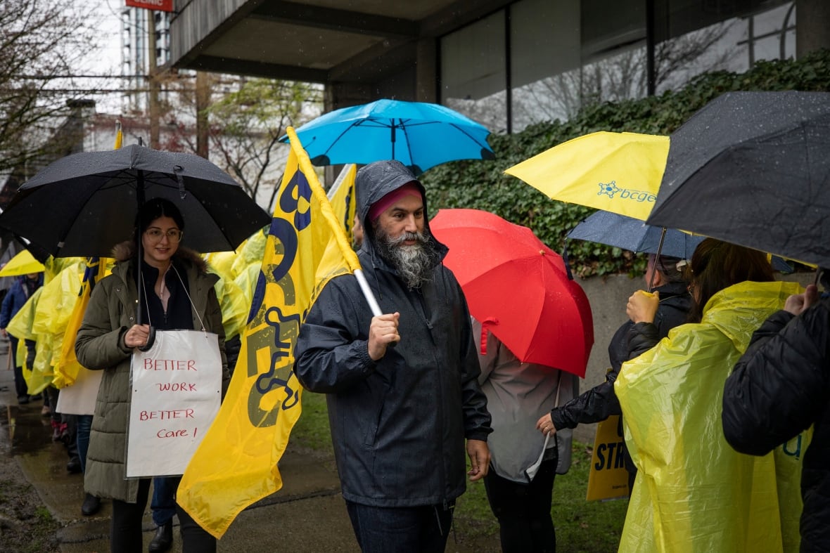 Jagmeet Singh holds a flag and walks in the rain with striking workers at Lifelabs in Vancouver BC.