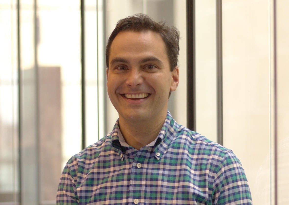 A man in a checkered shirt smiles in a posed photo.