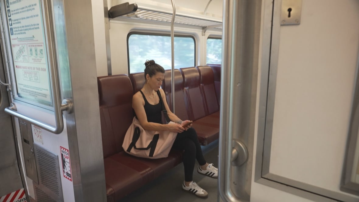 A woman sits on an empty train, looking down at her phone.