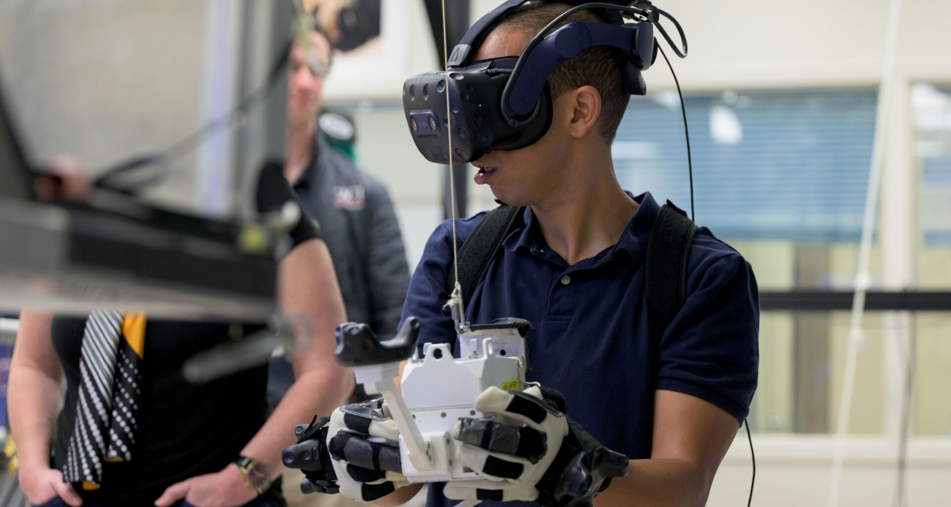 An astronaut wears a VR headset and holds controllers in his hands during a training exercise.