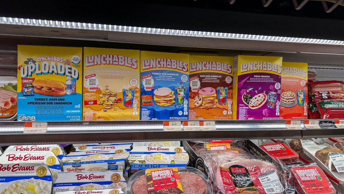 colourful boxes of packaged lunchable snacks are displayed on a fridge shelf in a grocery store. on the shelf below, you can see packaged cold cuts and mashed potatoes.