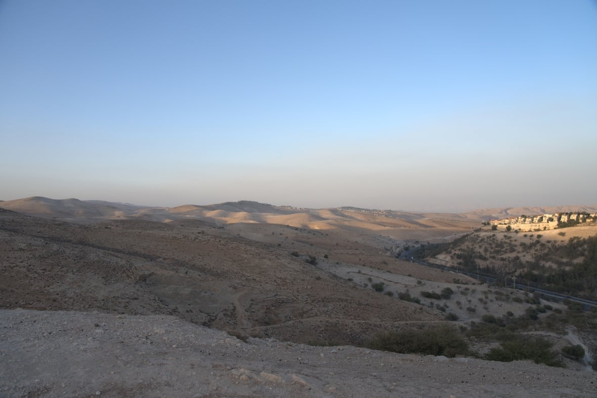 A wide shot of a hilly, desert landscape under a clear blue sky.