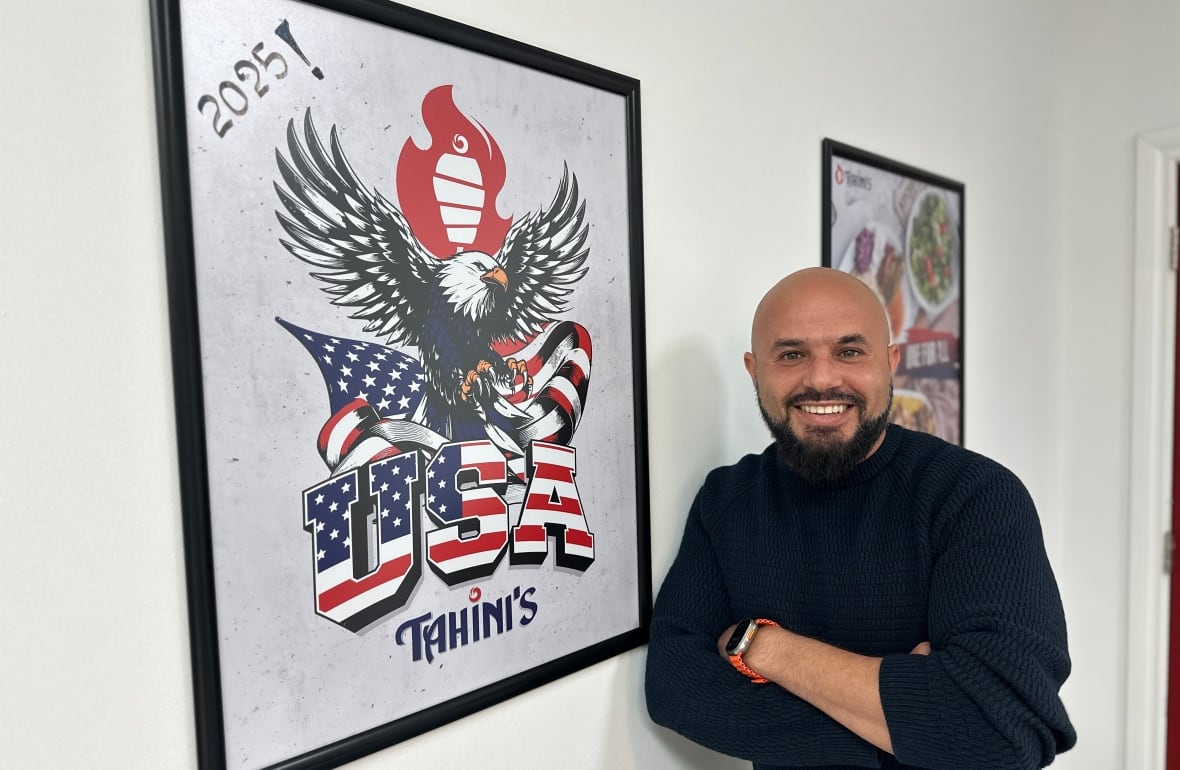 Omar Hamam, the owner of Tahini's, stands in front of a sign that shows the restaurant's name and the words USA and a giant bald eagle. 