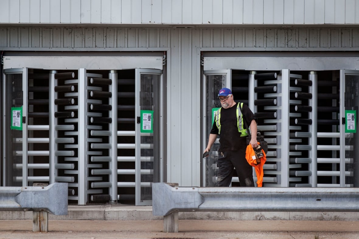Photo showing a man wearing black clothes and a reflective vest standing outside a factory. 