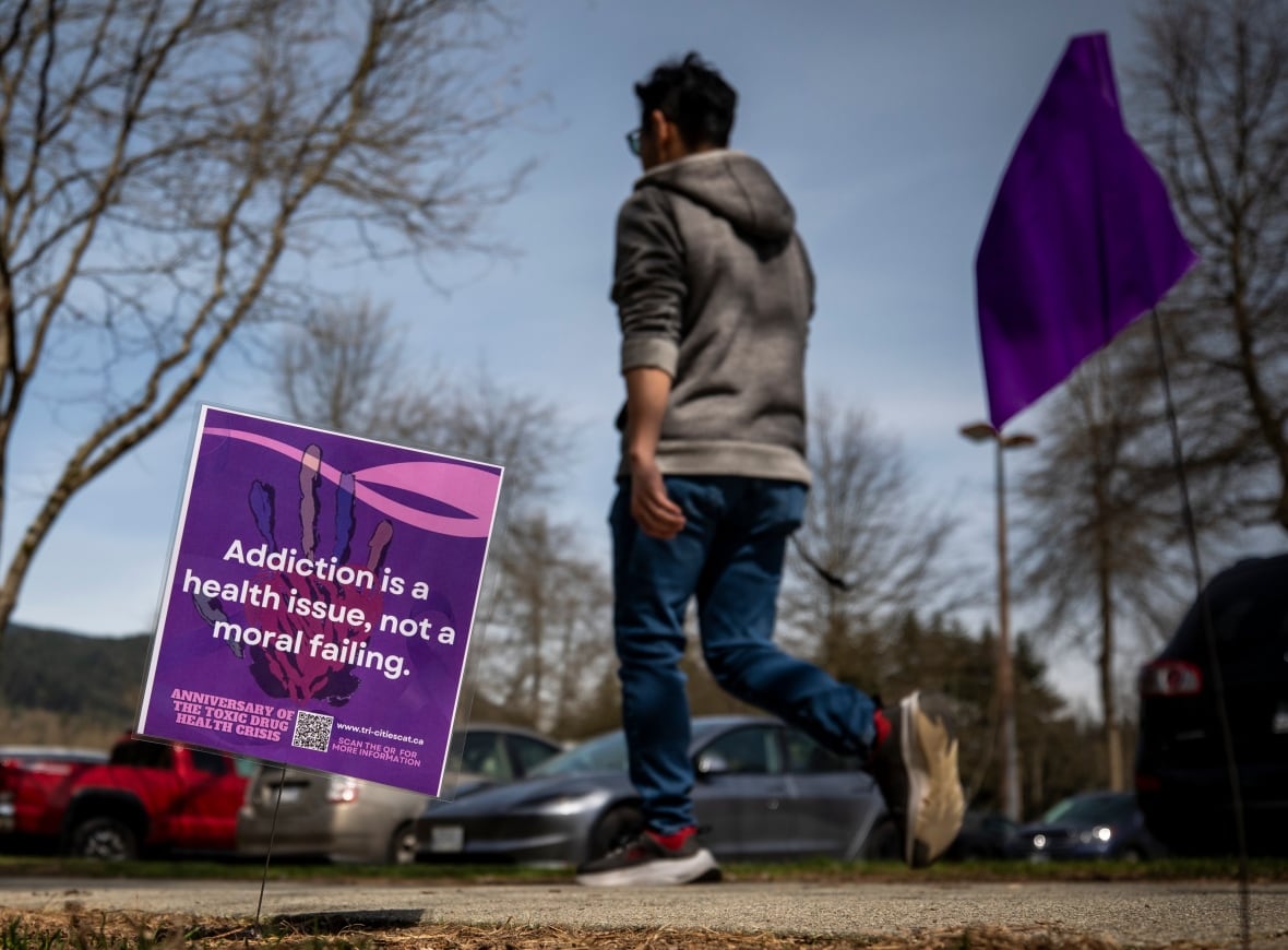 A person walks past a flag in the ground reading 'Addiction is a health issue, not a moral failing'.