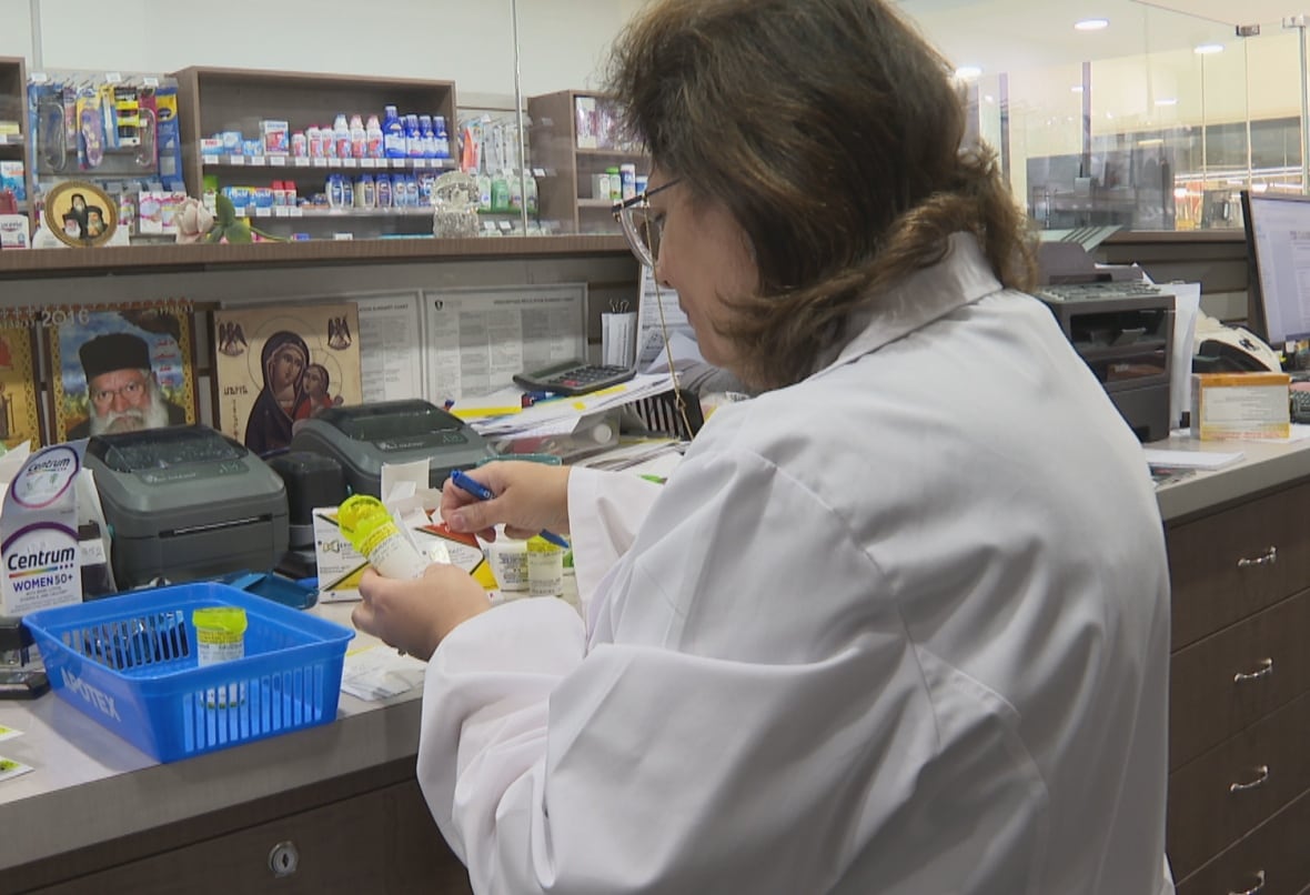 A pharmacist stands with her back turned to the camera as she places a label on a prescription botte.