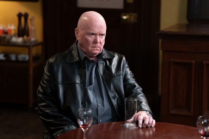 Steve McFadden as Phil Mitchell in EastEnders sat down at a table looking miserable.