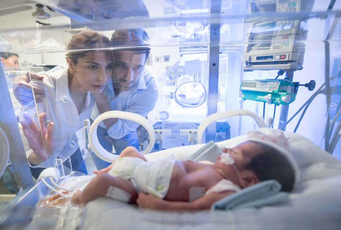 Worried young couple looking at their premature newborn in an incubator with oxygen at neonatal intensive care unit