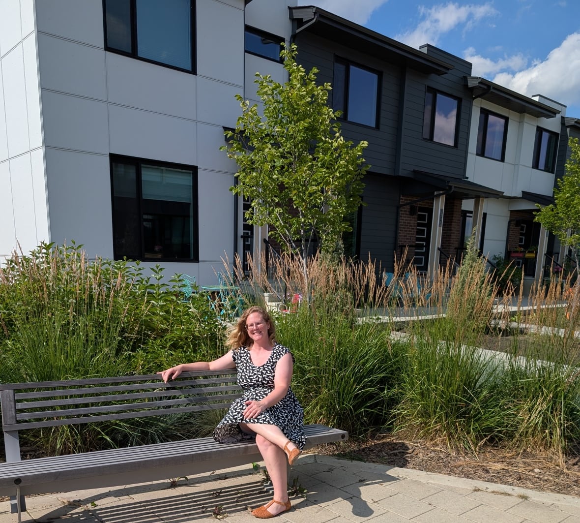 Woman sits on bench in front of row of townhouses