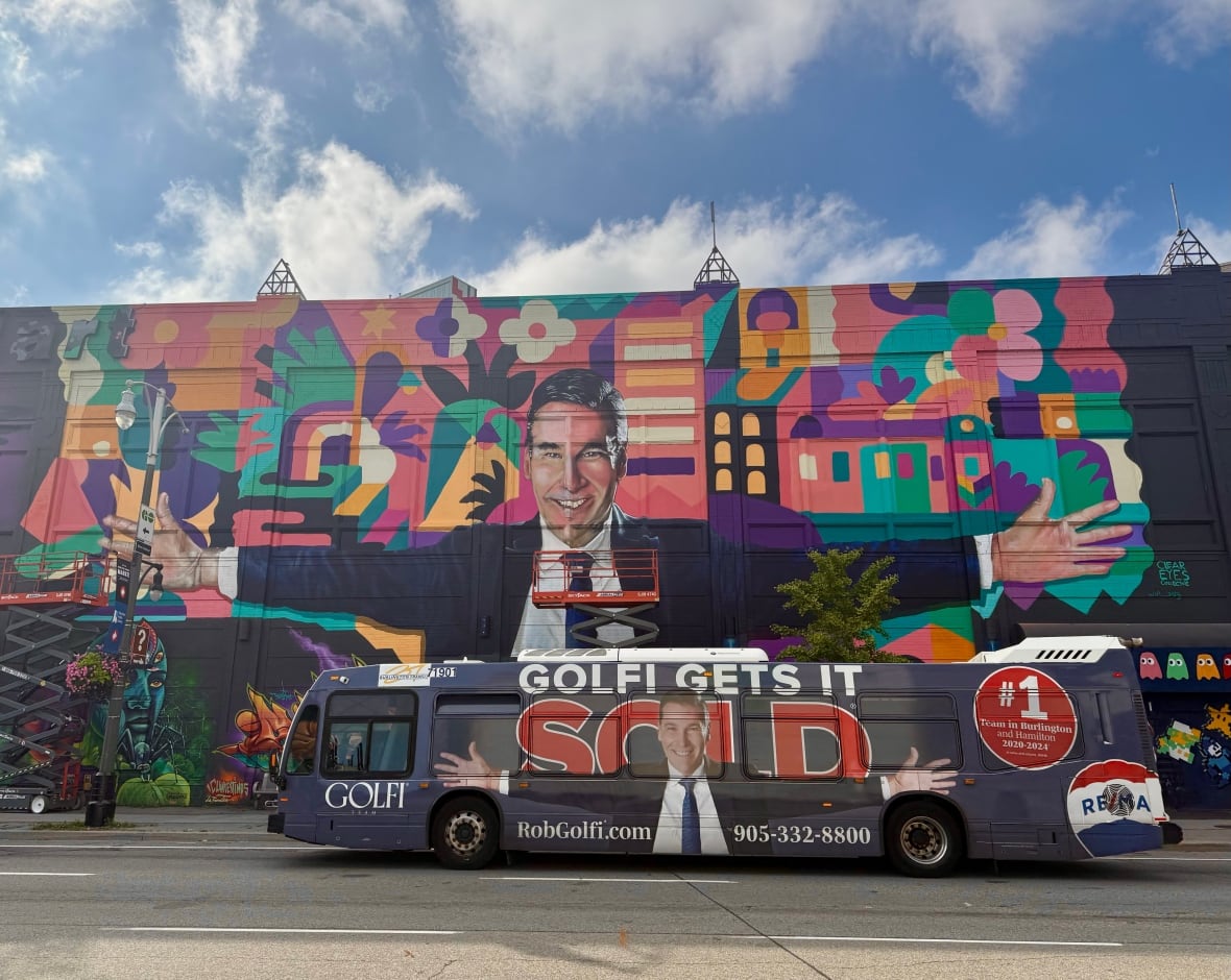 In the background, a mural of man with arms outstretched. In the foreground, a bus drives by with photo of same man with arms outstretched and the advertising "Golfi gets it sold."