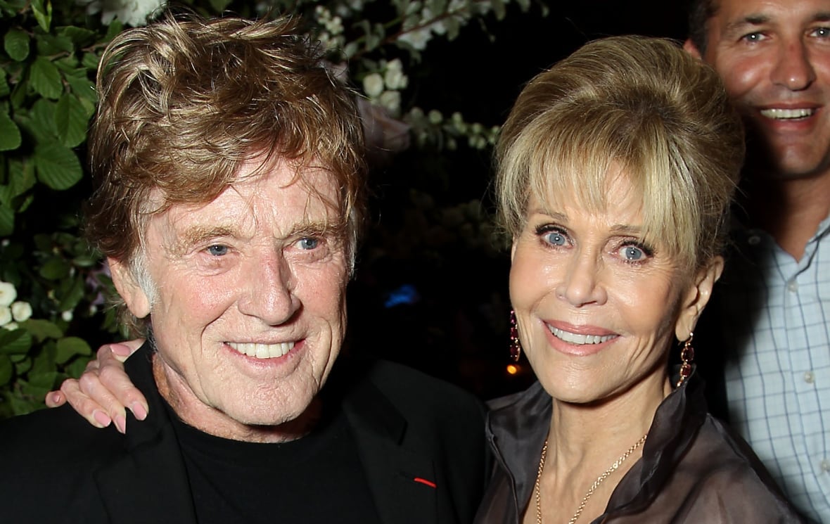 a blonde man on the left and a blonde woman on the right smile together on a red carpet