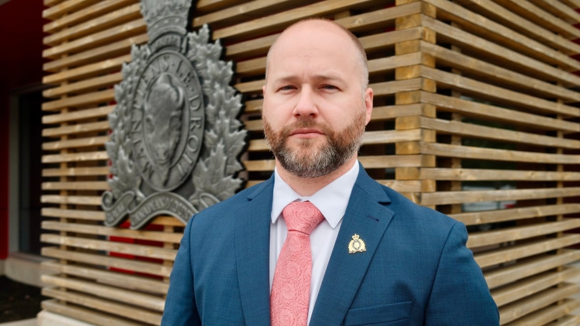 A man in a blue suit with a pink tie stands in front of an RCMP crest. 