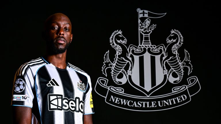 Yoane Wissa poses for photographs wearing a home shirt next to the club badge at the Newcastle United Training Centre