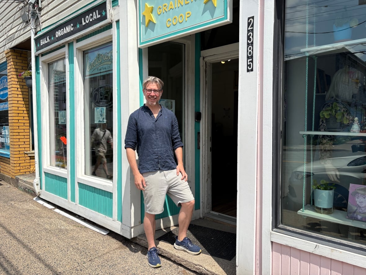 A man stands on the step of a storefront that has a sign over the door reading The Grainery Co-op.