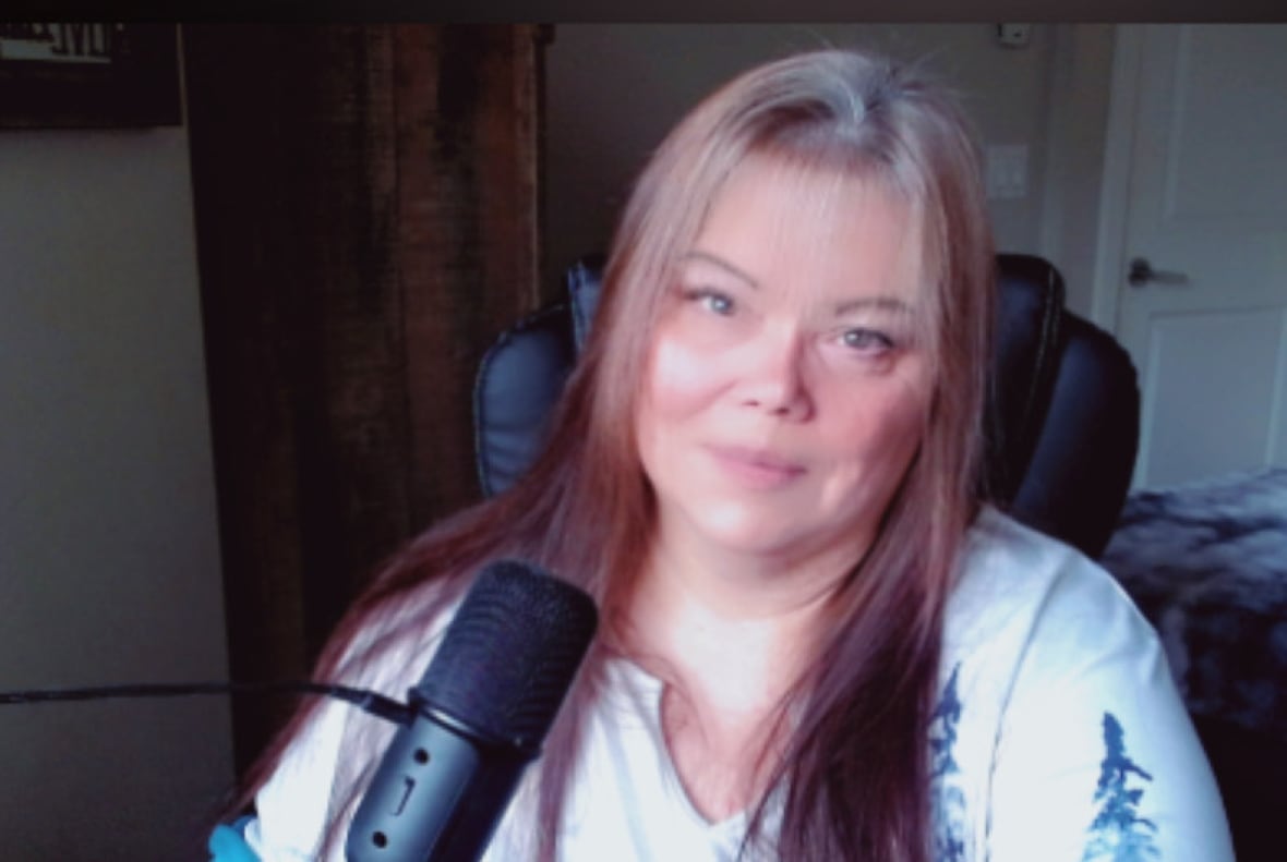 A woman in a white shirt and long hair sits in front of a microphone.