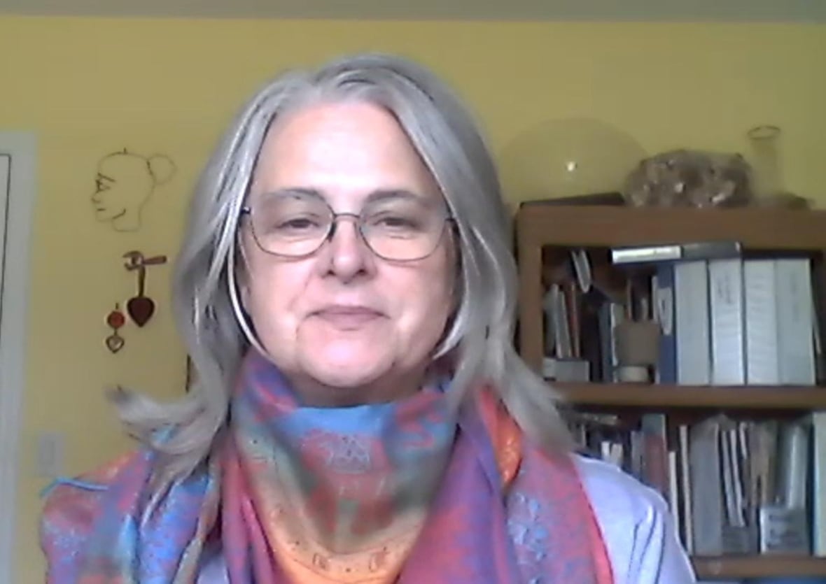 A woman wearing a patterned scarf smiles in a room with a bookcase behind her.