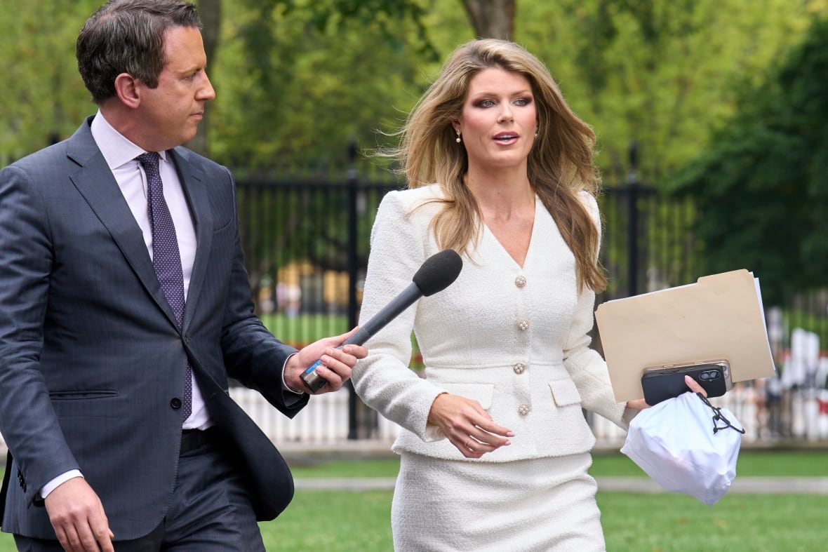 Man in a suit walks and holds a microphone out to a woman in a white suit 