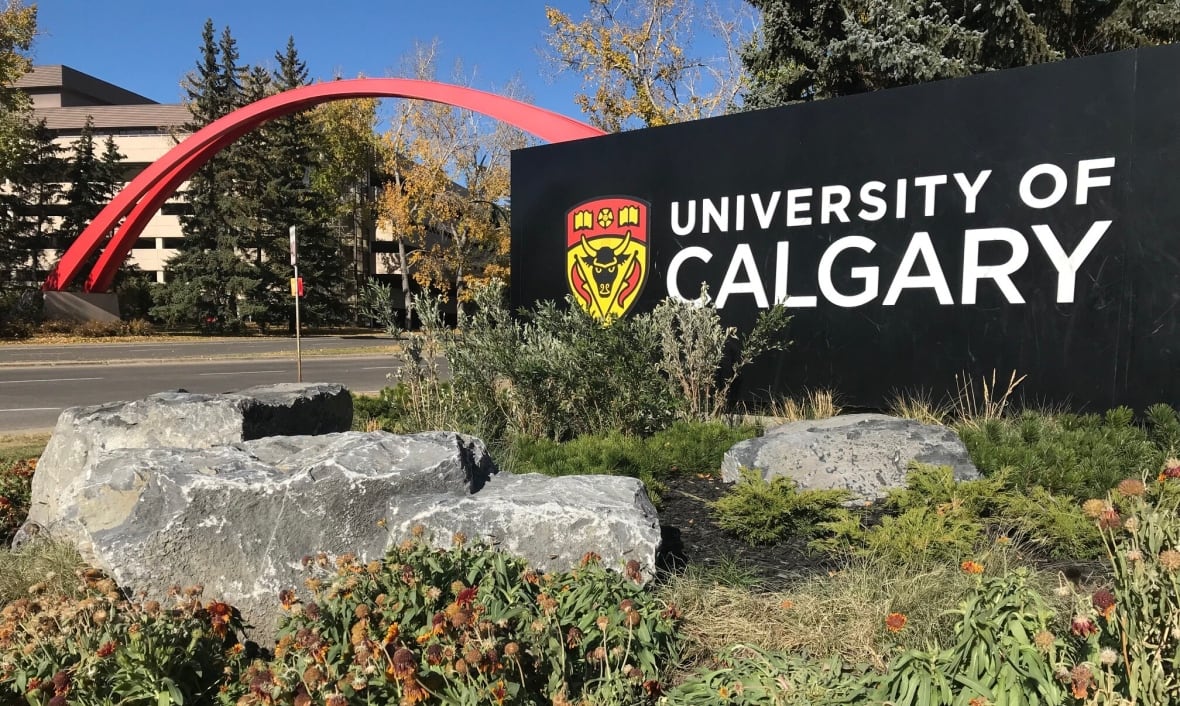 A black sign says University of Calgary. Behind it, a red archway stretches over a roadway.