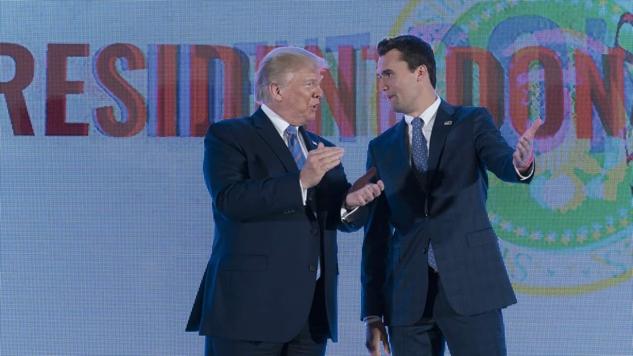 A man in a suit claps as he is greeted by another man in a suit on a stage.