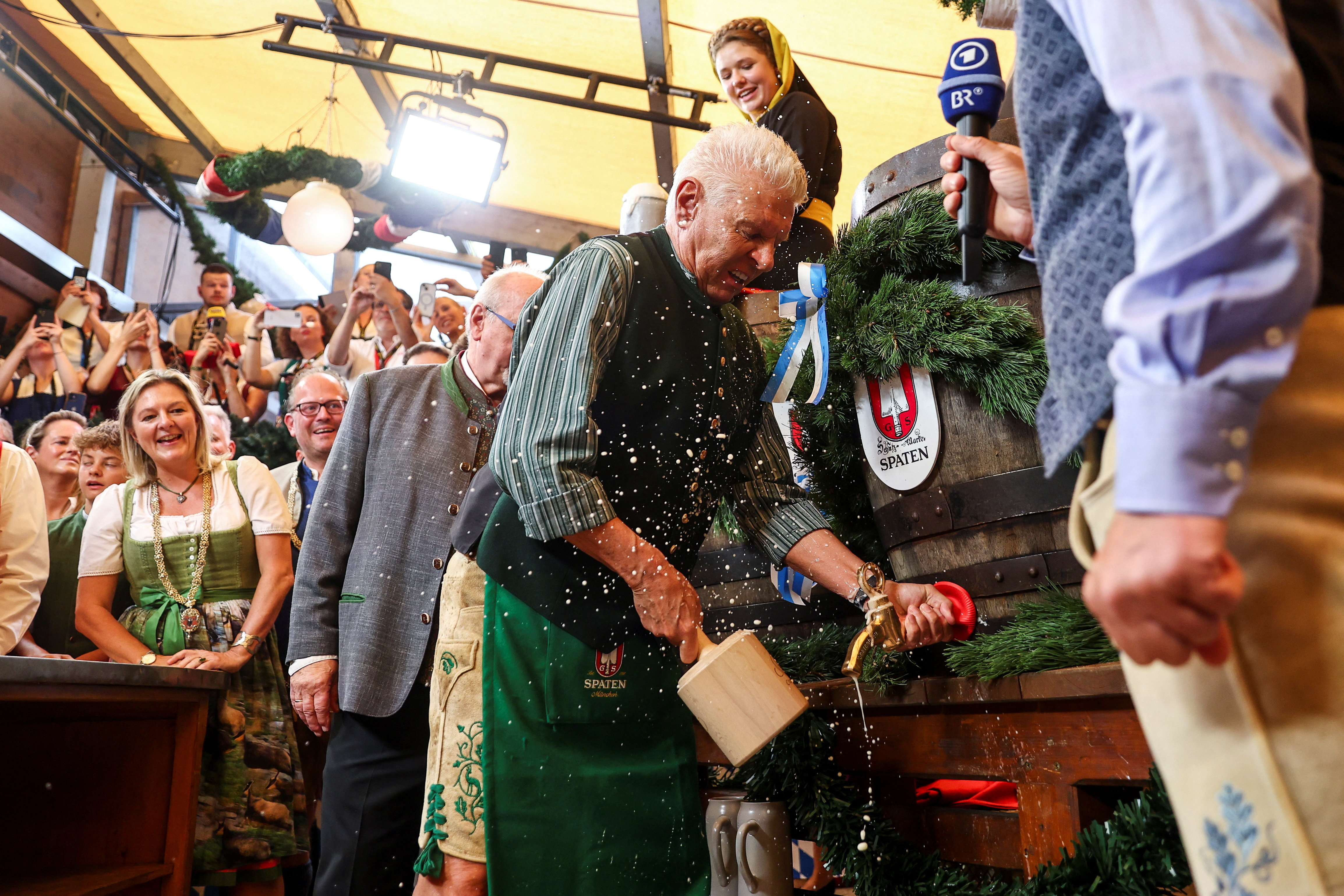 Mayor Dieter Reiter taps the first barrel of beer at the 190th Oktoberfest, spilling foam as spectators record on phones.