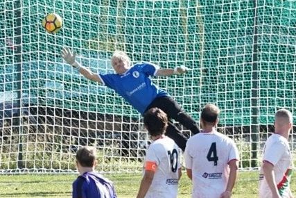 Lamberto Boranga, a goalkeeper, diving to catch a soccer ball in front of the goal.