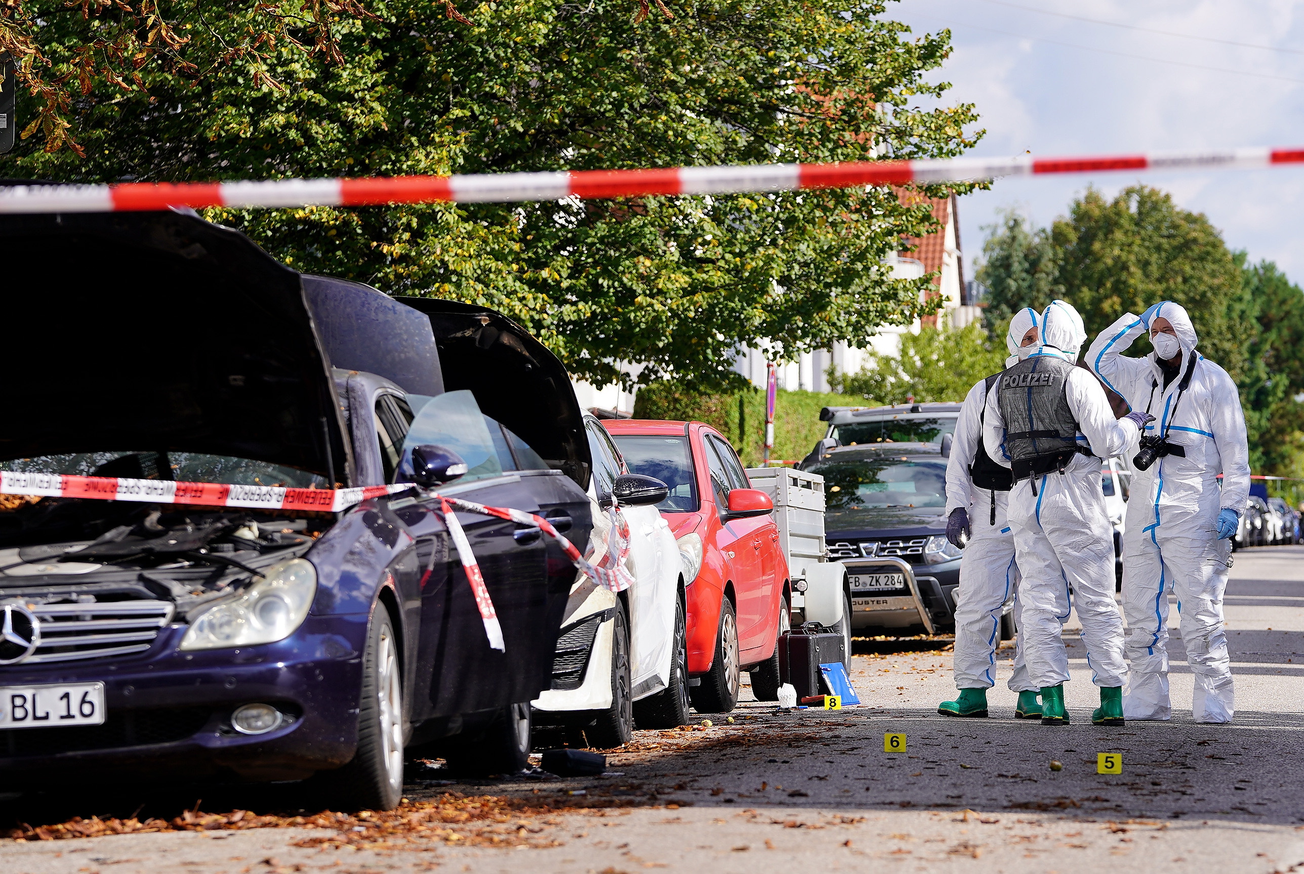 Police officers from a forensic unit work near damaged vehicles.